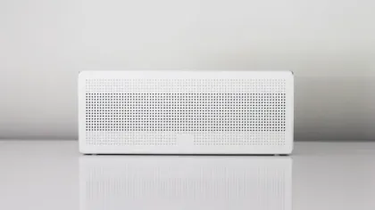 White rectangular Bluetooth speaker with perforated front panel on a reflective surface against a gray background