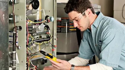 Technician in safety glasses using a multimeter to check HVAC system wiring and components indoors