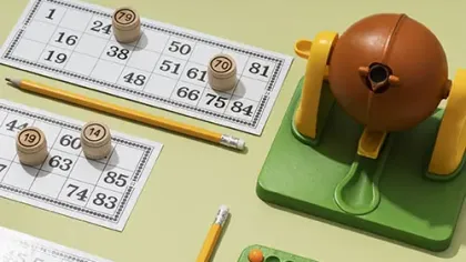 Bingo game setup with cards, wooden number markers, yellow pencils, and a green and brown ball cage dispenser.
