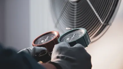 HVAC technician wearing gloves adjusting pressure gauges near air conditioning unit fan.