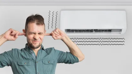 Man in green shirt plugging ears from loud noise of white wall-mounted air conditioner