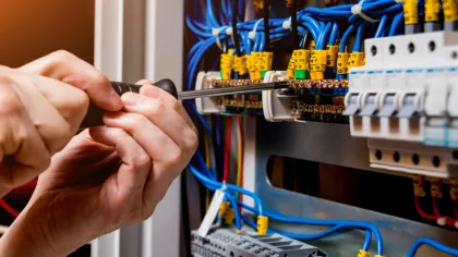 Electrician tightening screws on circuit breaker panel with blue wires in industrial electrical cabinet