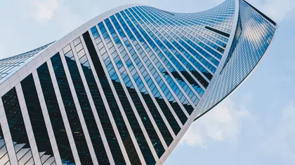 Twisting modern skyscraper with glass windows reflecting sky and clouds in an urban setting