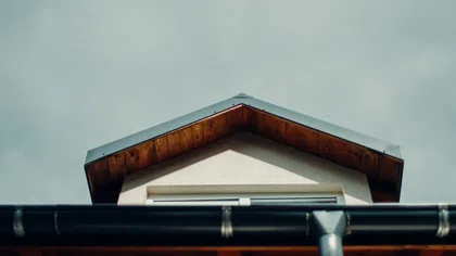 Close-up of a house rooftop with wooden eaves and a black gutter against a cloudy sky.