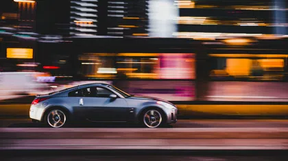 Silver sports car speeding past blurred city lights at night creating dynamic motion effect
