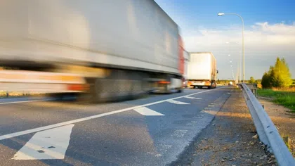 Blurred trucks moving fast on a highway with clear skies and roadside guardrails in the evening light