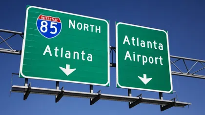 Green highway signs for Interstate 85 North to Atlanta and Atlanta Airport against clear blue sky.