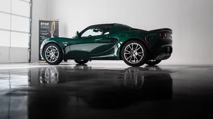 Dark green sports car parked indoors with glossy floor reflecting the vehicle side profile and wheels.