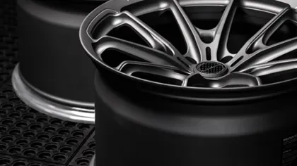 Close-up of two matte black alloy car wheels with intricate spoke design on a textured surface.