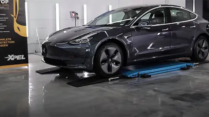 Dark gray Tesla Model 3 on a car lift in a garage with XPEL protection banner in the background