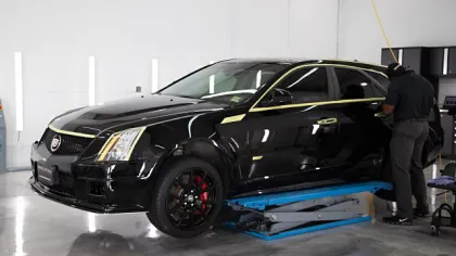 Person working on a black luxury car inside a bright garage with polished concrete floor and equipment.