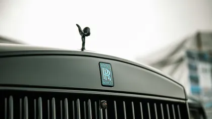 Close-up of the Rolls-Royce emblem and Spirit of Ecstasy hood ornament on a black luxury car grille.