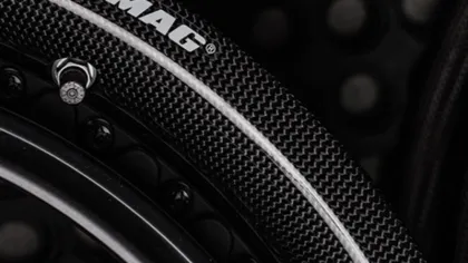 Close-up of a DYMAG carbon fiber motorcycle wheel rim with tire valve and textured surface.