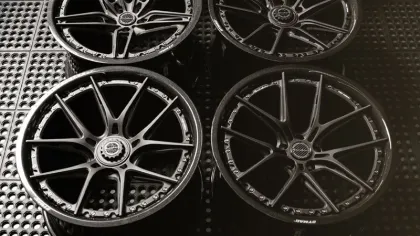 Set of four black multi-spoke alloy car wheels displayed on a perforated black surface.