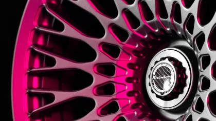 Close-up of a silver car wheel rim with intricate spokes and pink lighting accents against a black background