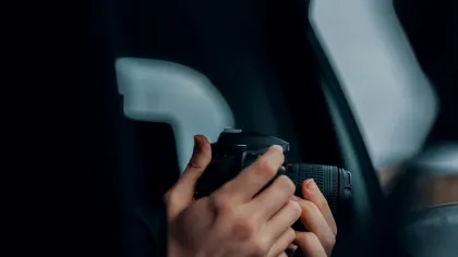 Hands holding a camera inside a vehicle near the window in low light environment focused on photography.