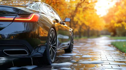 Black luxury car parked on a wet cobblestone road during autumn with orange leaves and sunset.