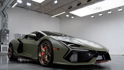 Matte green luxury sports car with red brake calipers in a bright modern garage with industrial lighting.