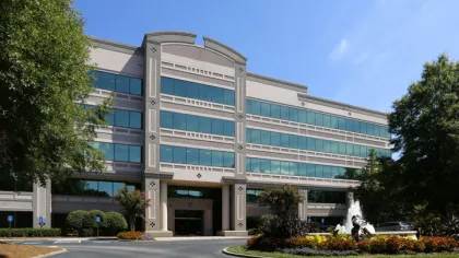 Modern office building with large windows and landscaped roundabout fountain under clear blue sky