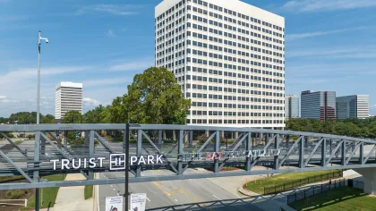 Truist Park sign on a metal pedestrian bridge with Atlanta office buildings and blue sky in the background