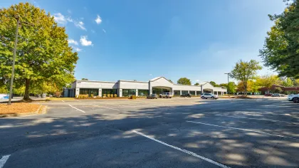 Wide view of a mostly empty parking lot with a low commercial building and clear blue sky on a sunny day.