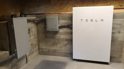 Tesla Powerwall home battery system installed in a concrete utility room with electrical panels.