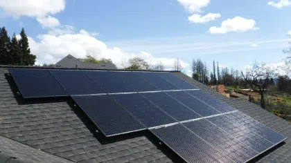 Solar panels installed on a shingled rooftop under a partly cloudy blue sky