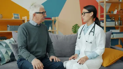 Elderly man and female doctor having a consultation sitting on a couch in a colorful room.