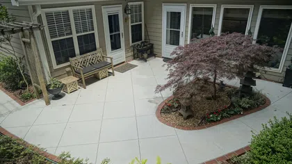 Spacious backyard patio with concrete flooring, wooden bench, small table, and landscaped garden area.