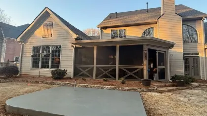 Concrete slab freshly poured in backyard near screened porch and two-story beige home on a clear day