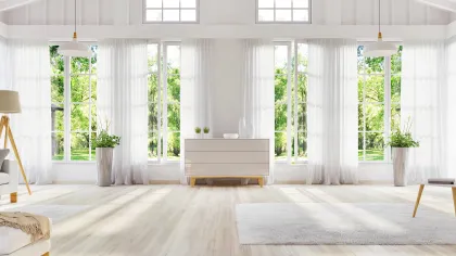 Bright modern living room with large windows, white curtains, light wooden floor, and minimalist furniture.