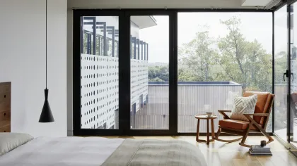 Modern bedroom with large glass sliding doors, wooden floor, leather chair, and minimalist decor.