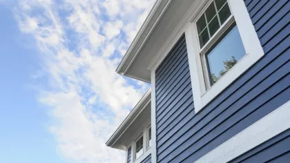 Blue house exterior with white trim and windows under a partly cloudy sky