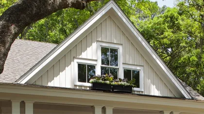 White house gable with triple windows and flower boxes surrounded by green trees and branches