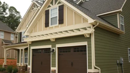Green suburban house with beige trim, double brown garage doors, and stone accents on the foundation.