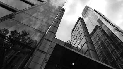 Black and white photo looking up at modern glass skyscrapers with cloudy sky reflecting on building surfaces