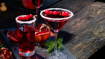 Red cocktails garnished with cranberries and rimmed with sugar on a rustic wooden table with pomegranate seeds.