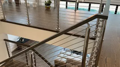 Modern interior with stainless steel cable railing, wood flooring, large windows, and indoor plants by stairs.