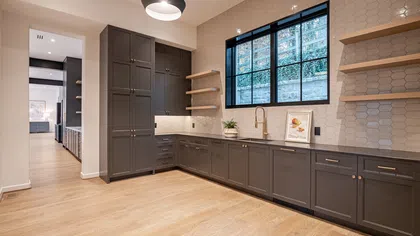 Modern kitchen with dark cabinetry, hexagonal tile backsplash, large window, and light wood flooring.