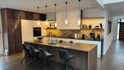 Modern kitchen with marble backsplash, large island, pendant lights, and four gray bar stools on wooden floor