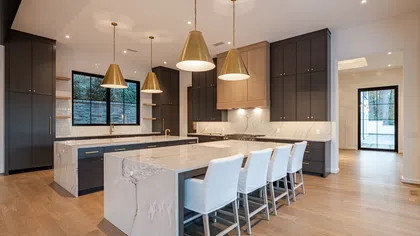 Modern kitchen with marble island, navy cabinets, gold pendant lights, white chairs, and hardwood floors