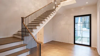 Modern interior with wooden staircase, black metal railing, hardwood floor, and glass door leading outside.