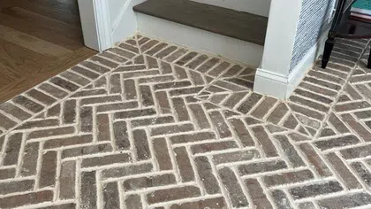 Indoor corner with dark wooden stairs and brick floor laid in herringbone pattern near a patterned wall.