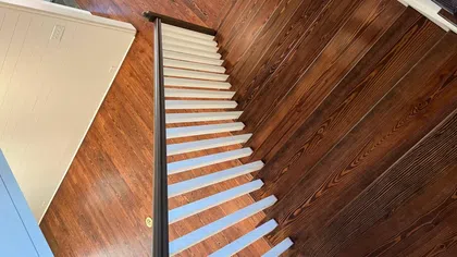 Top view of a wooden staircase with white steps, dark handrail, and polished hardwood floor below.