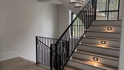 Modern staircase with wooden steps, black decorative metal railing, and built-in step lighting in bright interior.