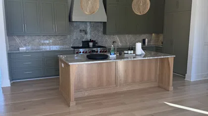 Modern kitchen with green cabinets, wooden island, marble countertops, and two pendant lights over the island.