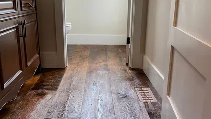 Dark rustic hardwood floor in a hallway with light-colored walls and white-trimmed window and door frames.
