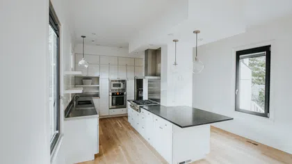Bright modern kitchen with white cabinetry, black countertops, stainless steel appliances, and hardwood flooring