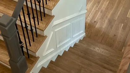 Interior wooden staircase with black iron balusters and white paneled wall details in a modern home.