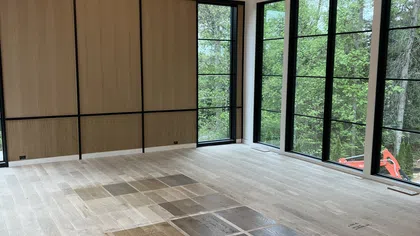 Bright room with large windows, wood panel wall, chandelier, and wood floor samples arranged in the center.